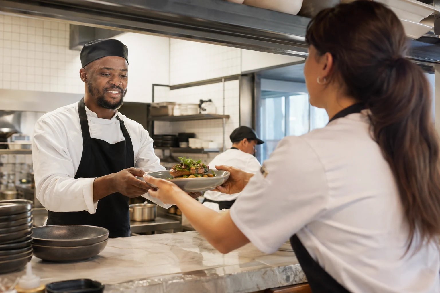 Chef receiving a completed plate from colleague at restaurant pass.